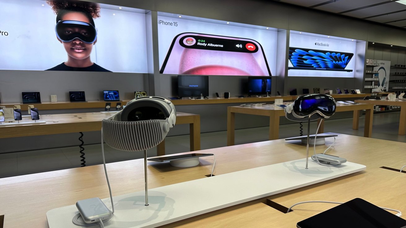 Интерьер розничного магазина Apple в Рокуэе, штат Нью-Джерси, с двумя гарнитурами Apple Vision Pro на деревянном столе.