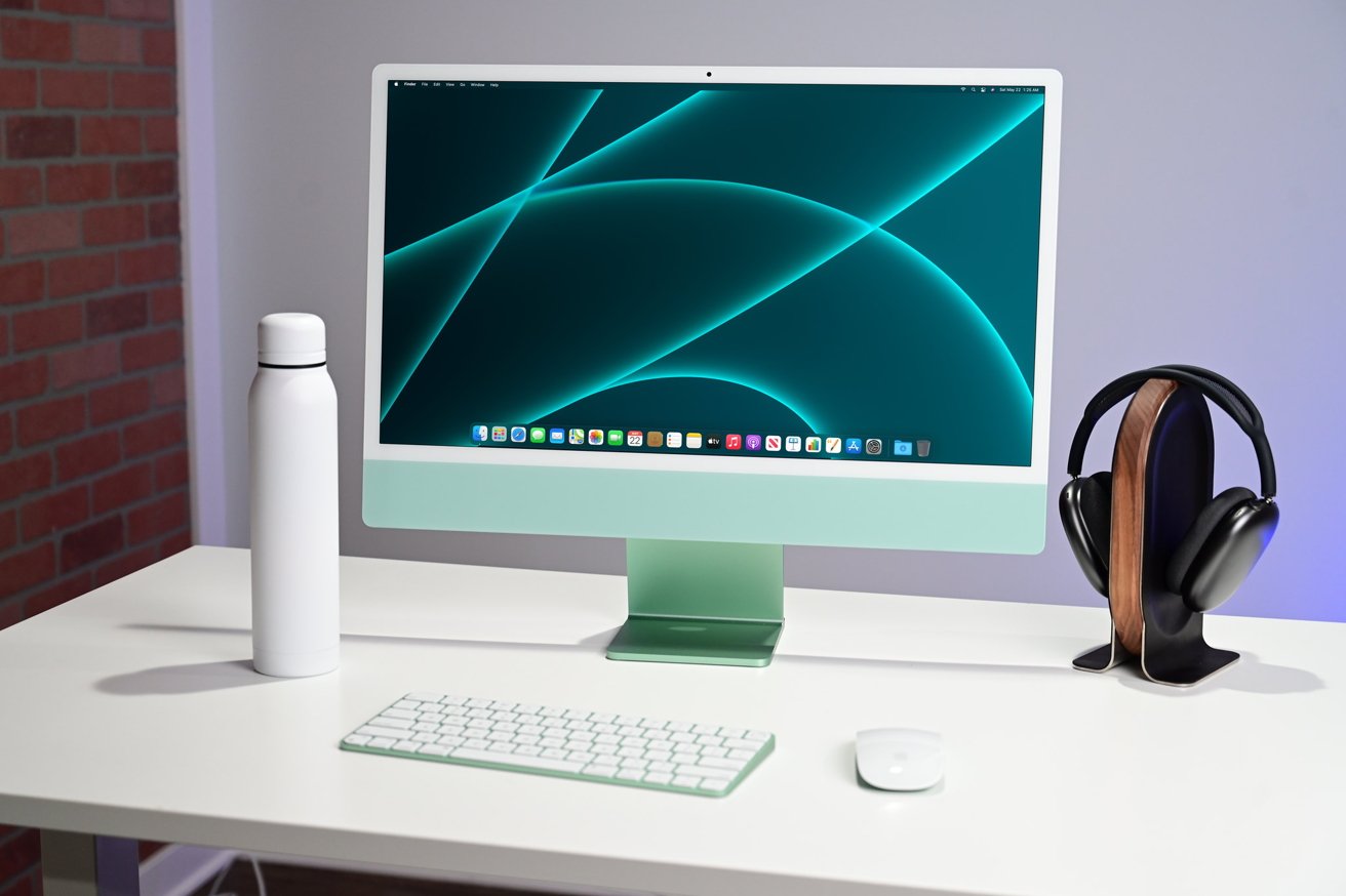 iMac с минималистской комплектацией, включая клавиатуру, мышь, бутылку с водой и наушники на белом столе.