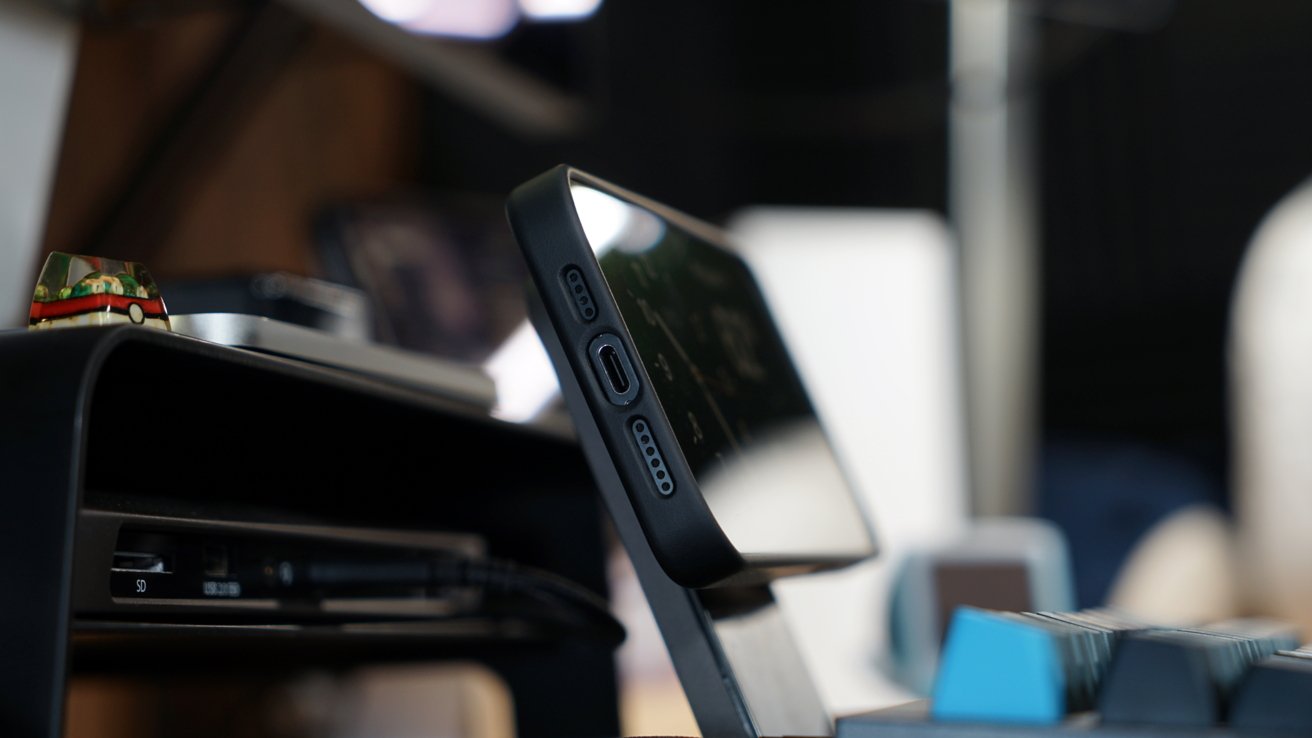 iPhone 15 Pro Max в чехле Torras на подставке MagSafe за клавиатурой на столе.