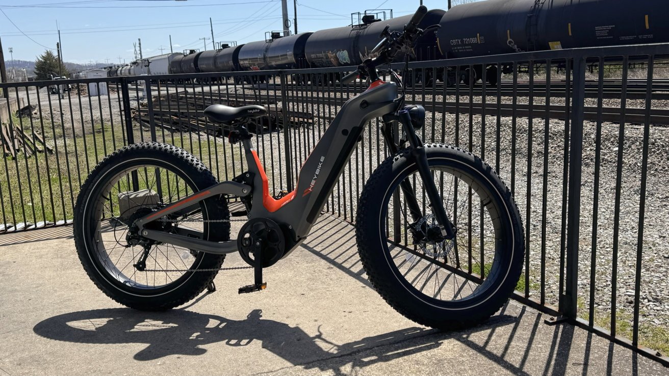 Heybike Hero припарковался у забора, на заднем плане проезжает поезд