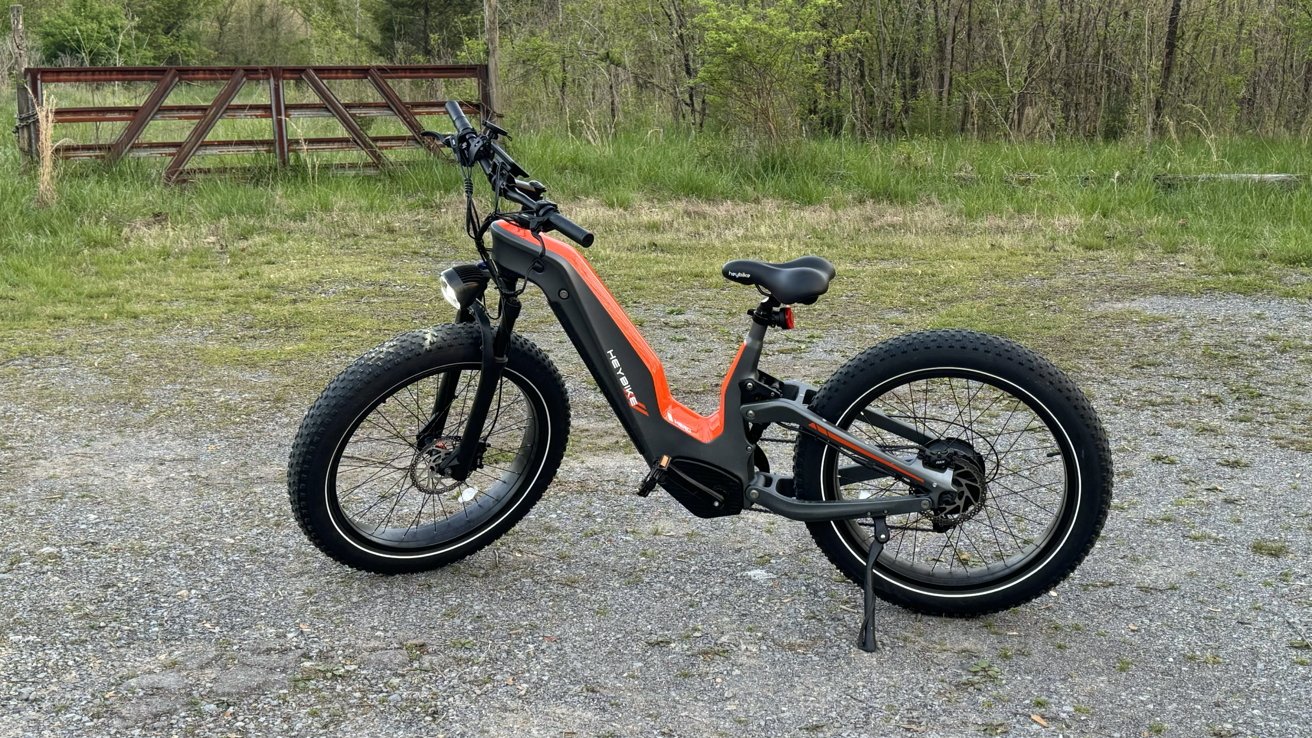 Heybike Hero на гравийной дорожке с дикой местностью и старыми воротами на заднем плане