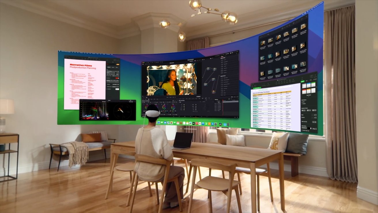 Женщина сидит за столом посреди комнаты, носит Vision Pro и большой виртуальный экран Mac, огибающий ее голову.