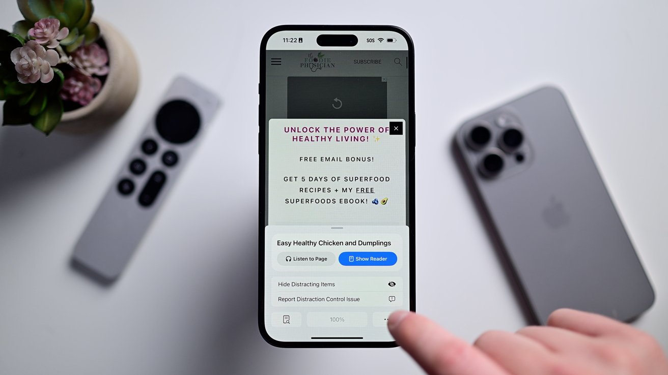 iPhone на белом столе с Safari. Внизу есть всплывающее окно с несколькими кнопками, включая кнопку для скрытия отвлекающих элементов.