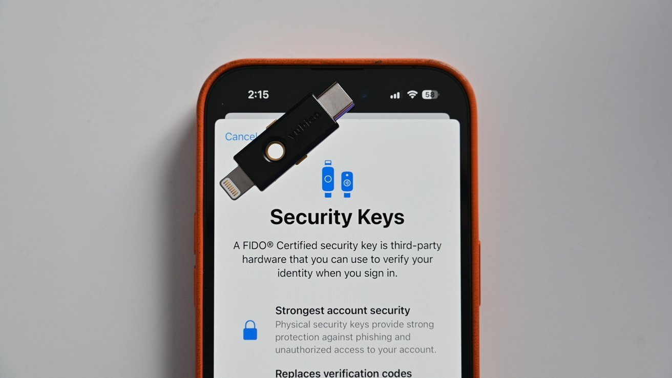 Экран iPhone, на котором отображается информация о ключах безопасности, с аппаратным ключом безопасности, размещенным на экране. Текст объясняет важность использования ключей безопасности для защиты учетной записи.