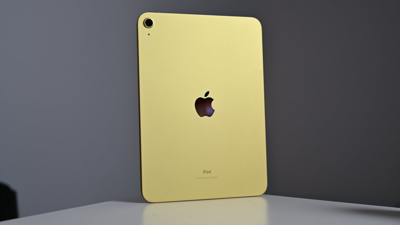 Желтый Apple iPad стоит вертикально на белой поверхности, видны камера и логотип Apple.