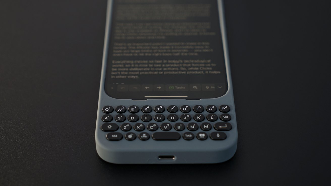 Смартфон с физической QWERTY-клавиатурой под сенсорным экраном, расположенный на темной поверхности.