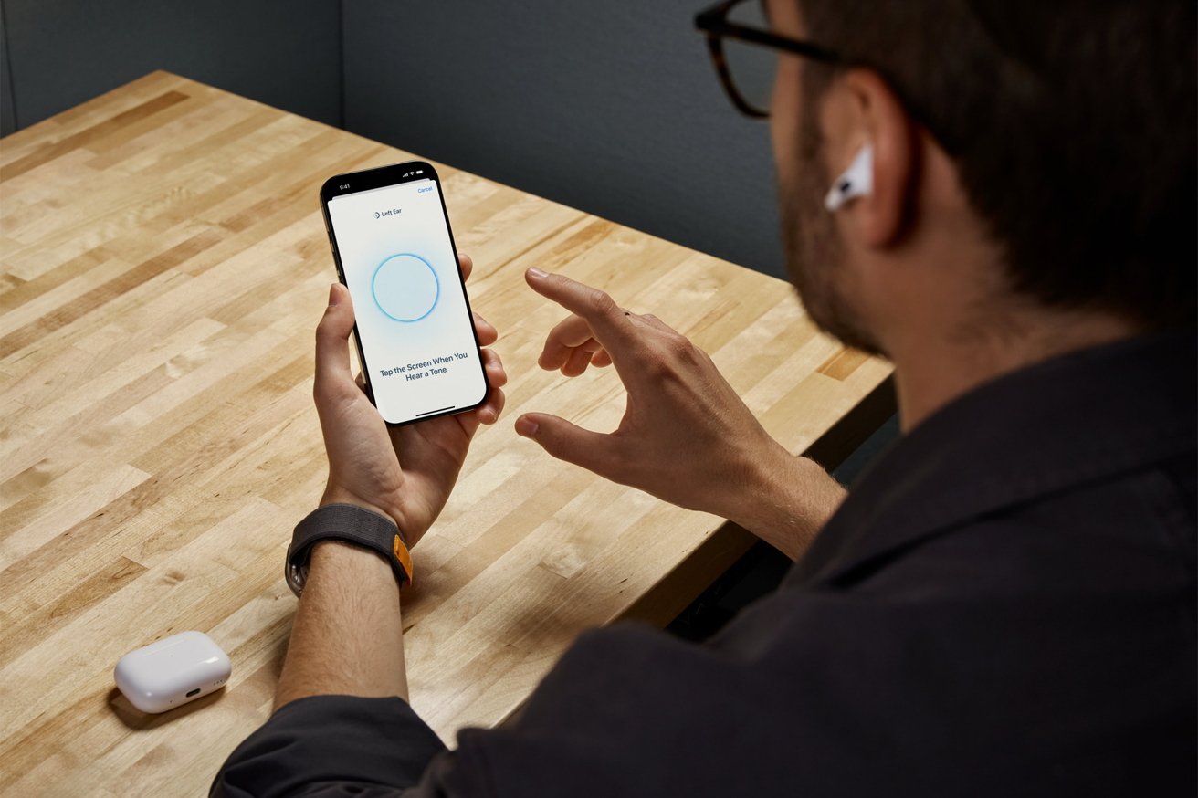 Человек с AirPods, использующий приложение для смартфона на деревянном столе, рядом с белым чехлом для зарядки.