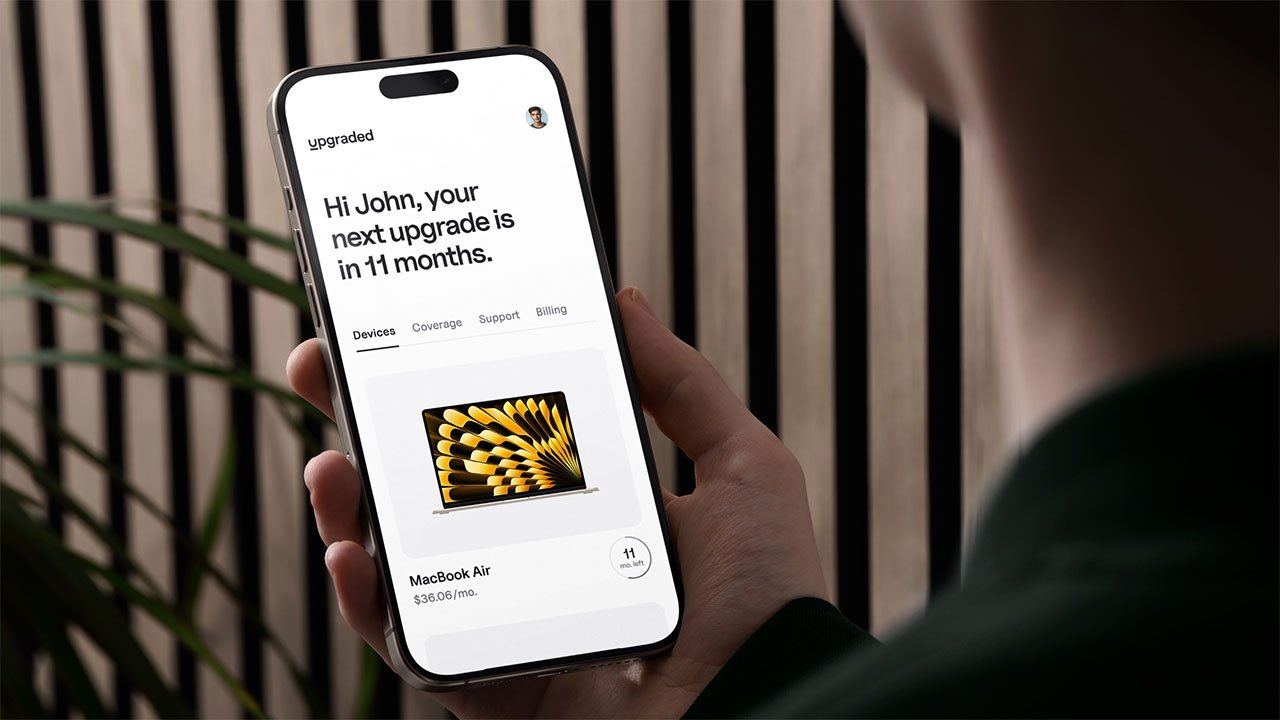 Человек, держащий iPhone, отображает уведомление об обновлении, а ниже показана реклама MacBook Air.