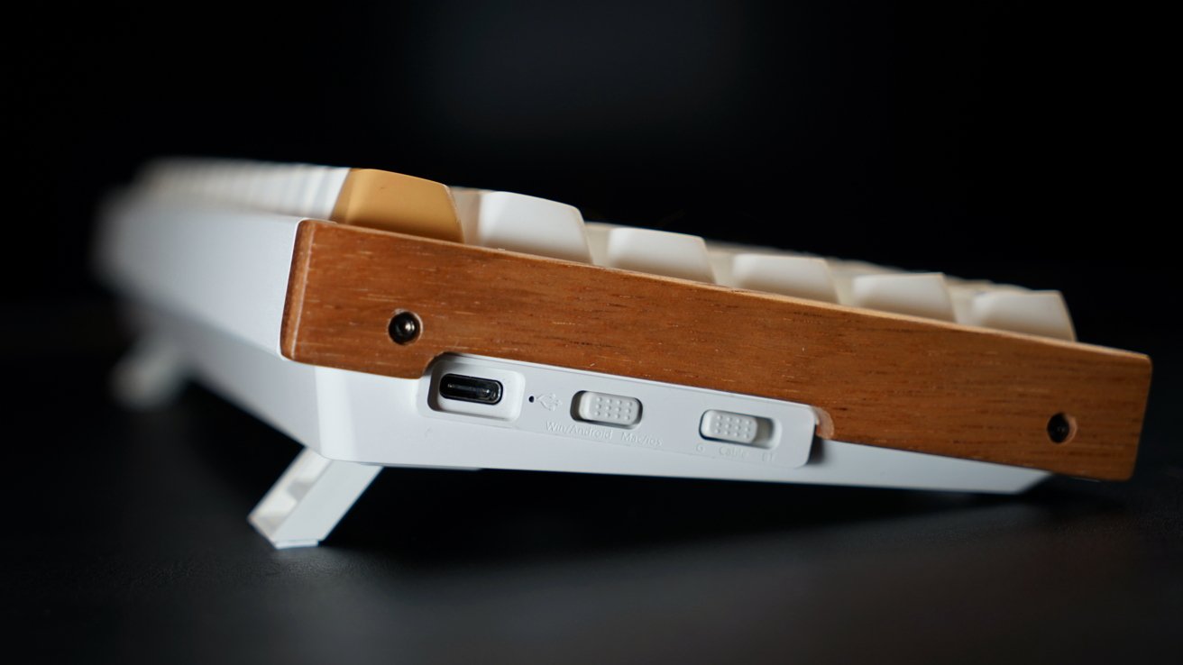 Белая клавиатура с деревянной боковой панелью, USB-портом, двумя тумблерами для выбора системы и режима на черной поверхности.