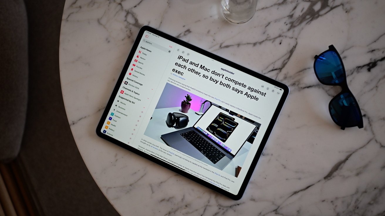 На планшете на мраморном столе отображается статья об iPad и MacBook, рядом с голубыми солнцезащитными очками.