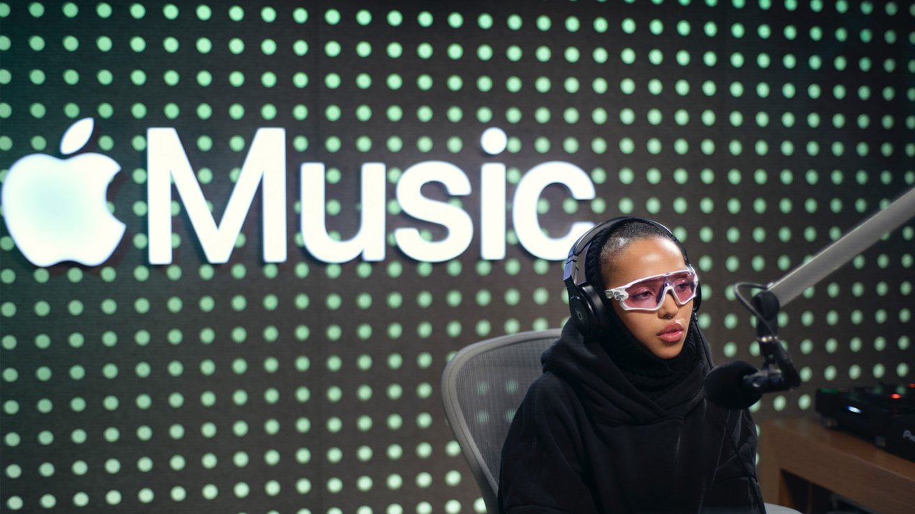 Женщина в наушниках и розовых очках говорит в микрофон на фоне логотипа Apple Music.