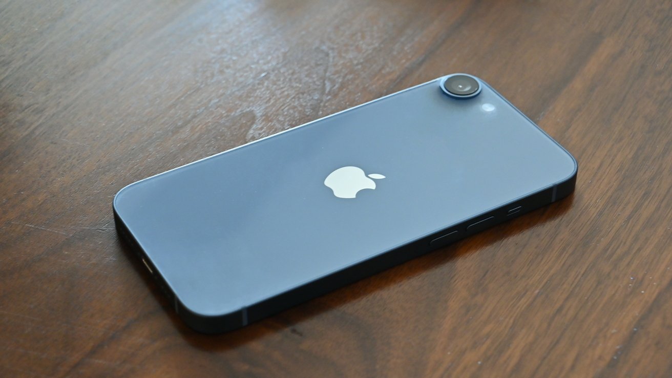 Смартфон с одинарной задней камерой и логотипом Apple, лежащий лицевой стороной вниз на деревянной поверхности.