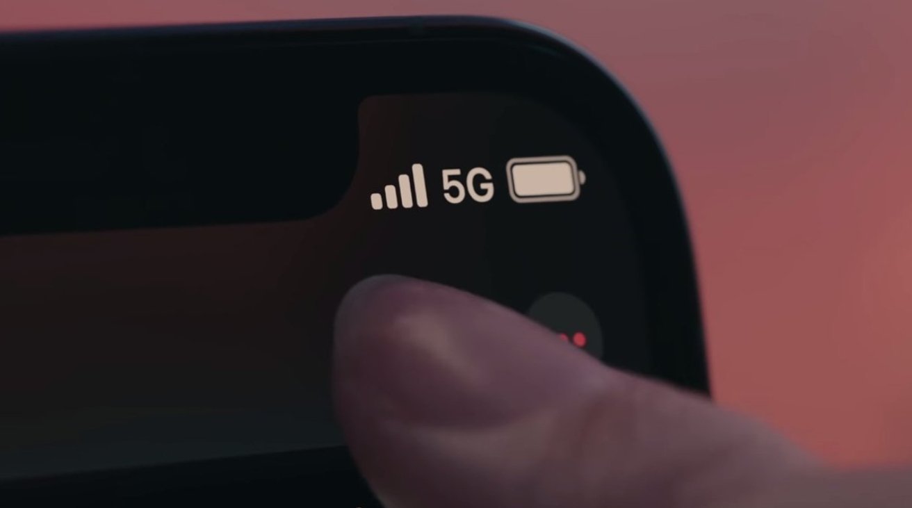 Крупный план угла экрана смартфона, на котором отображаются сигнал 5G, значок батареи и прикосновение пальца к экрану на размытом фоне.