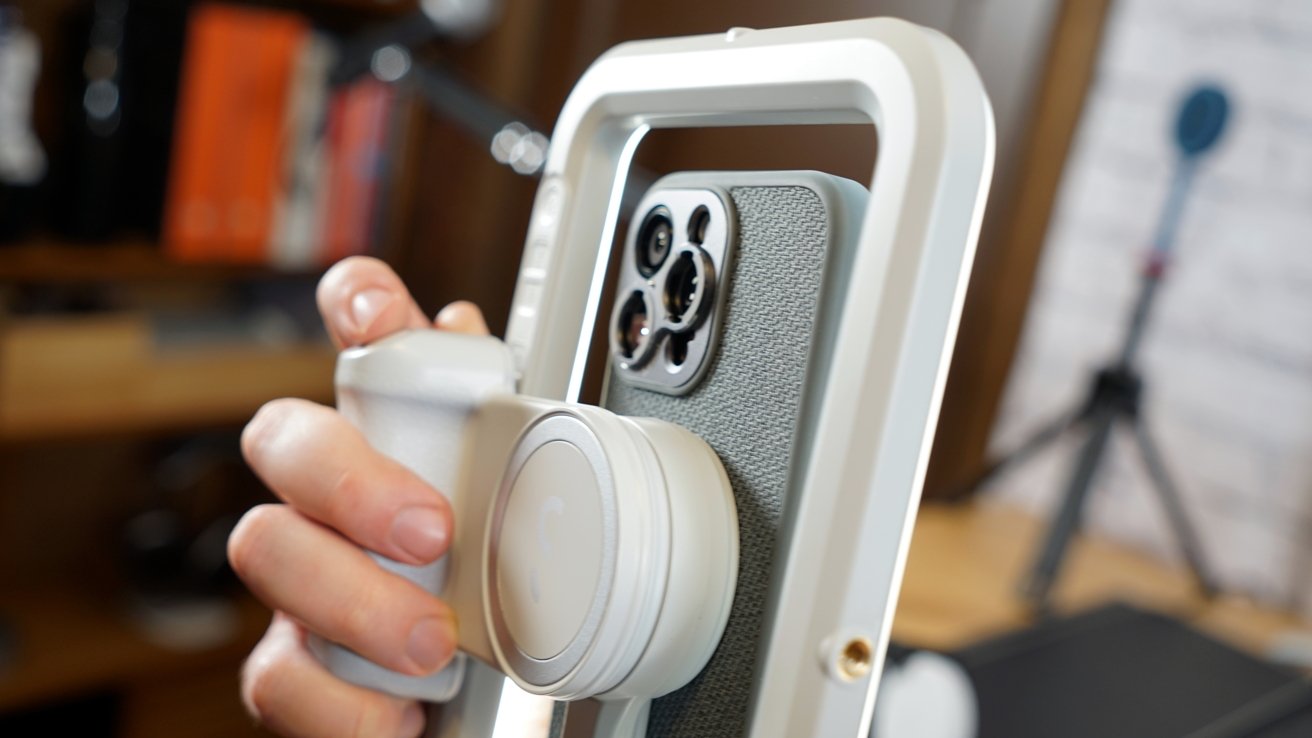 Рука держит смартфон, закрепленный на стабилизаторе gimbal, показывая камеру с несколькими объективами, с размытым фоном.