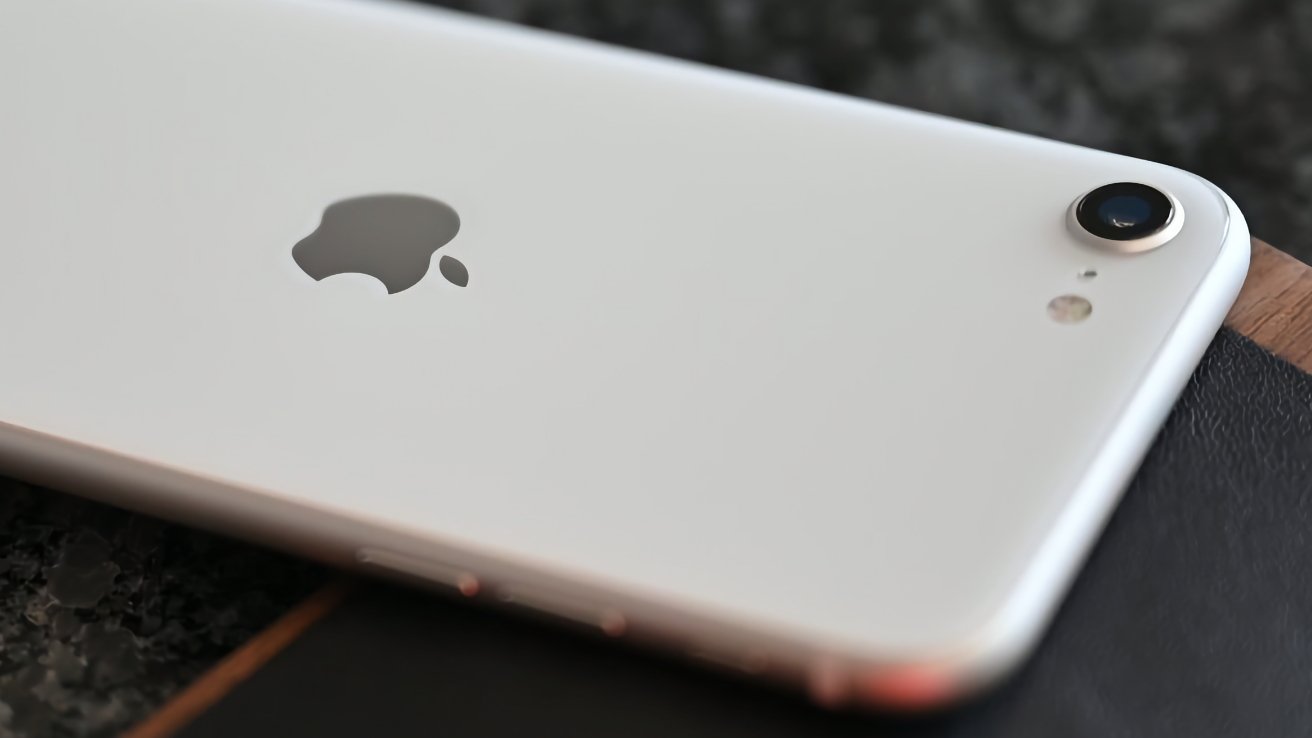 Крупный план белого смартфона с серебристым логотипом Apple и одинарной задней камерой на темной поверхности.
