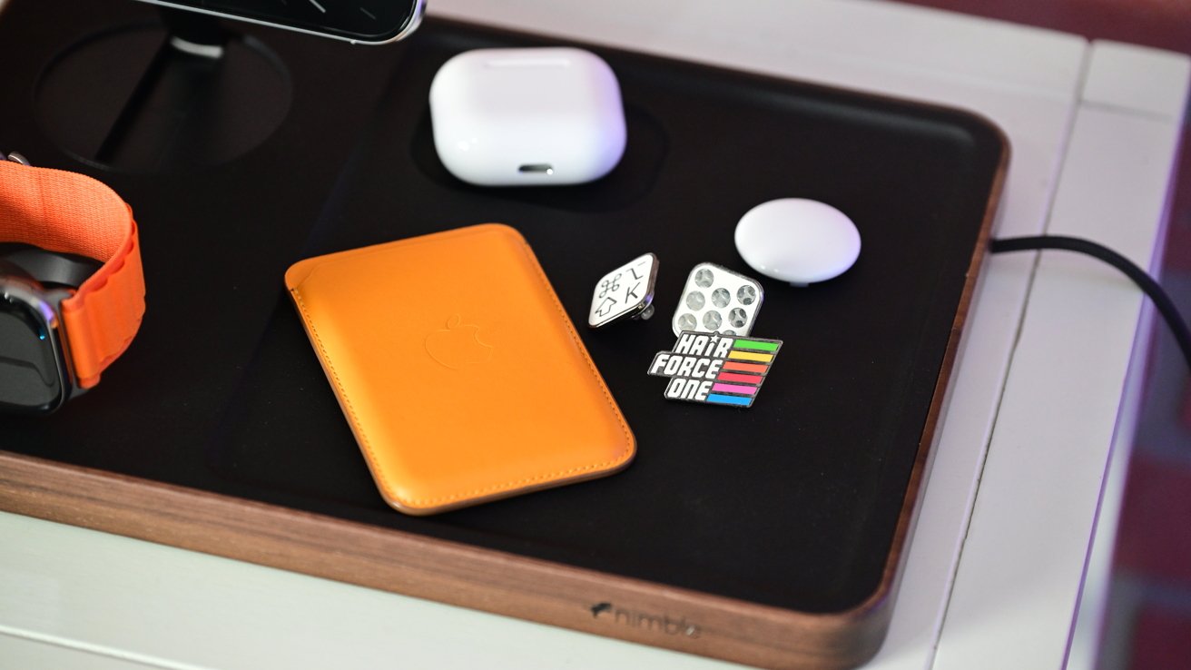 Зарядная станция с оранжевым бумажником, смарт-часами, чехлом AirPods, круглым ковриком и разноцветными булавками, включая надпись